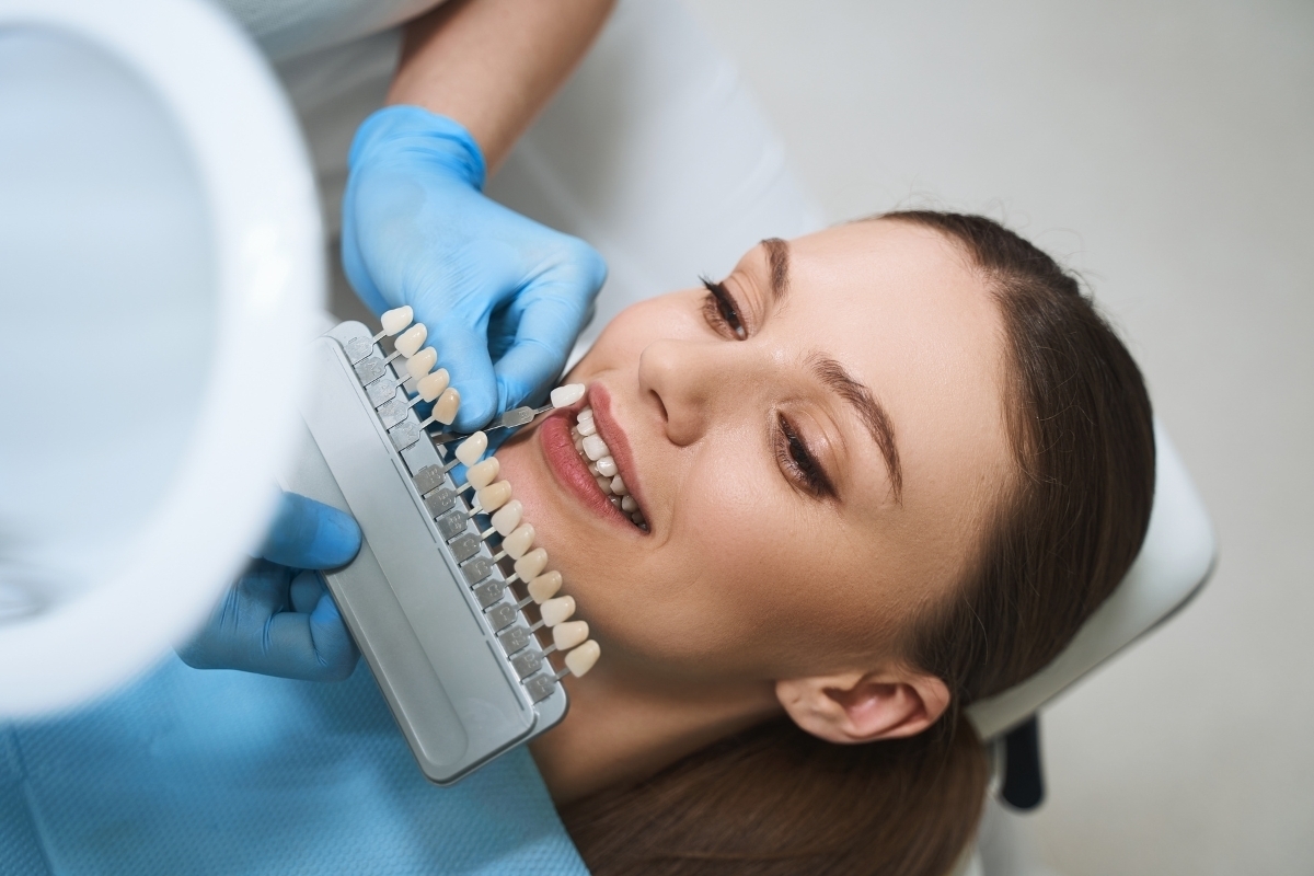 Dentist holding tooth shade guide next to patient's smile for veneer color matching.