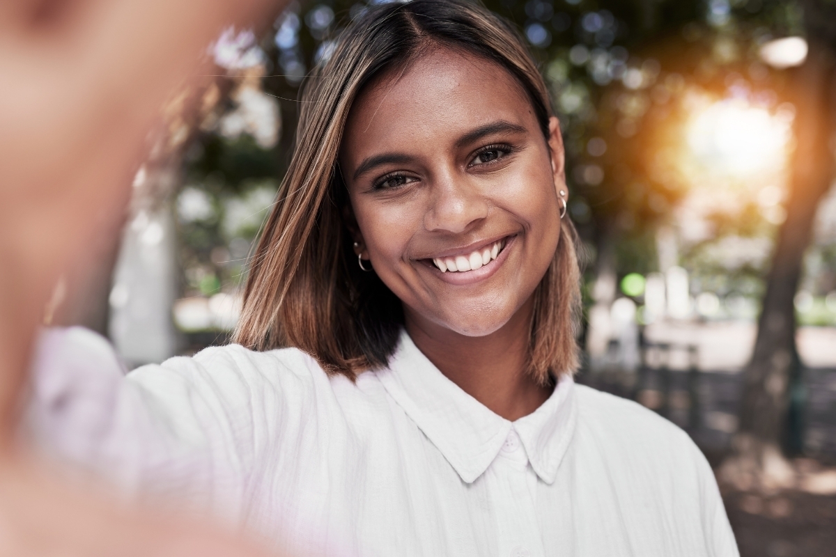 Smiling woman in white shirt outdoors showcasing natural-looking cosmetic dental results.