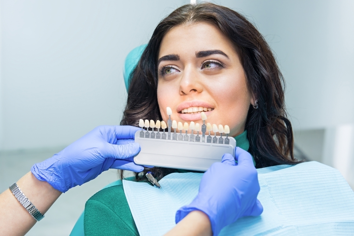 Dentist showing tooth shade guide to smiling patient during veneer consultation.