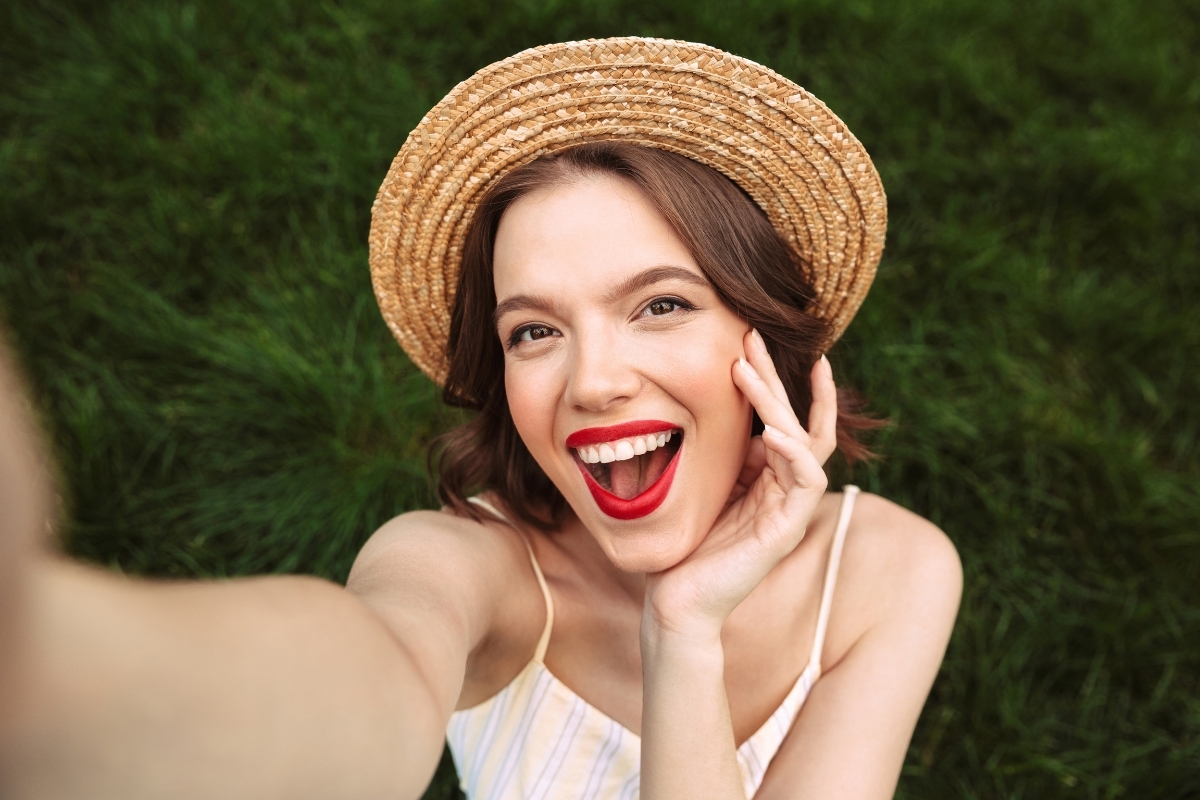 Woman with a bright white smile wearing a straw hat against a green backdrop.